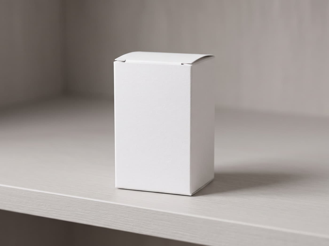 A plain white retail carton standing upright on a pale shelf in soft daylight.